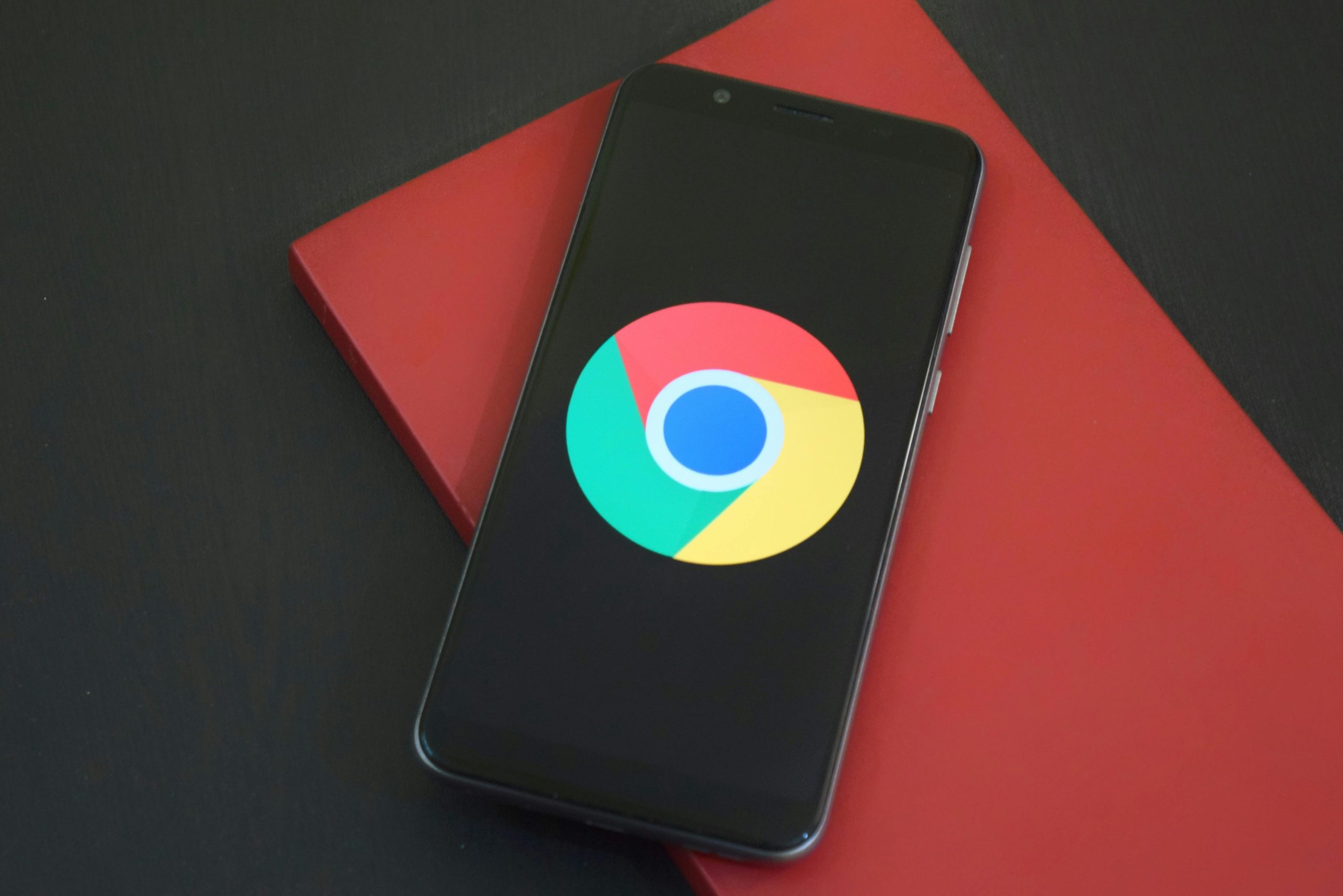 Close-up of a smartphone with Chrome browser logo on screen placed on a red notebook.